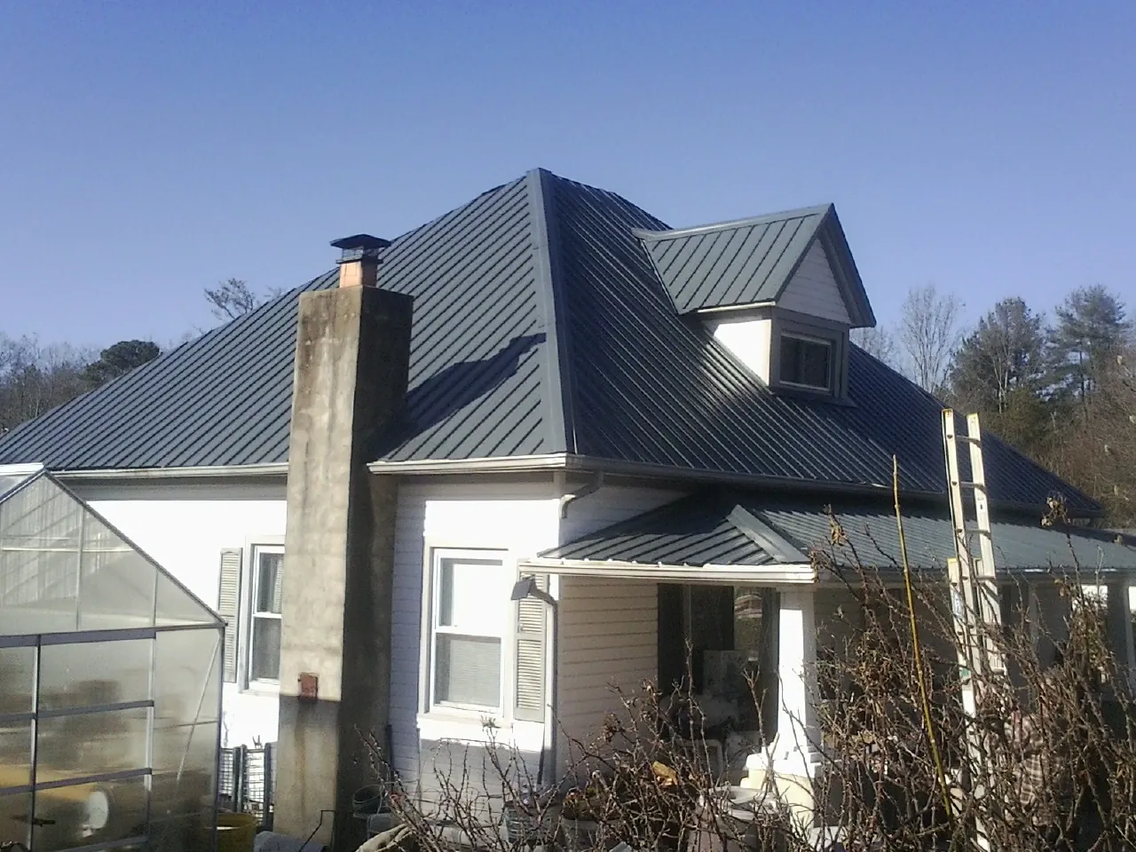 Dark blue standing seam metal roof on a white farmhouse with dormer — Slate & Tile Roof Repair by Roofing Brothers in Mc Cool Junction