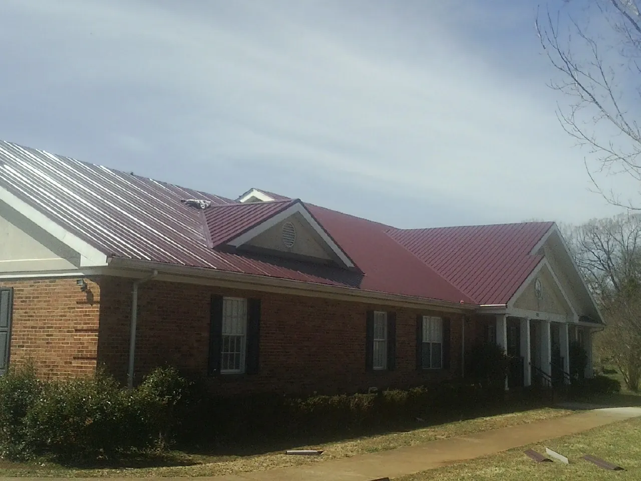 Red metal roof with gabled entries on a long brick building, from a Hail Damage Roof Repair job in Mc Cool Junction