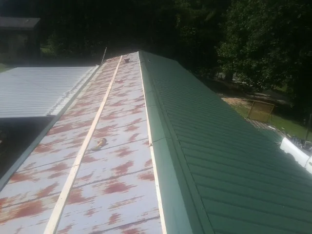 Old rusted panels beside newly installed green metal roofing — Wind Damage Roof Repair by Roofing Brothers in Mc Cool Junction