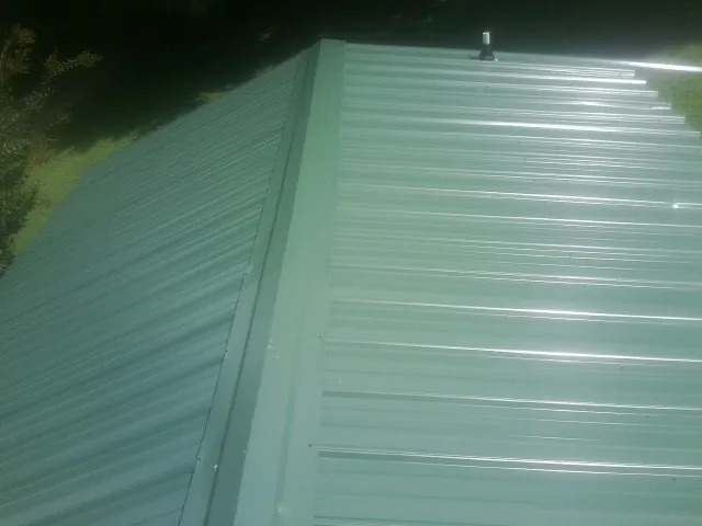 New green metal panels meeting at the ridge of a roof — Flat Roof Repair work by our crew in Mc Cool Junction