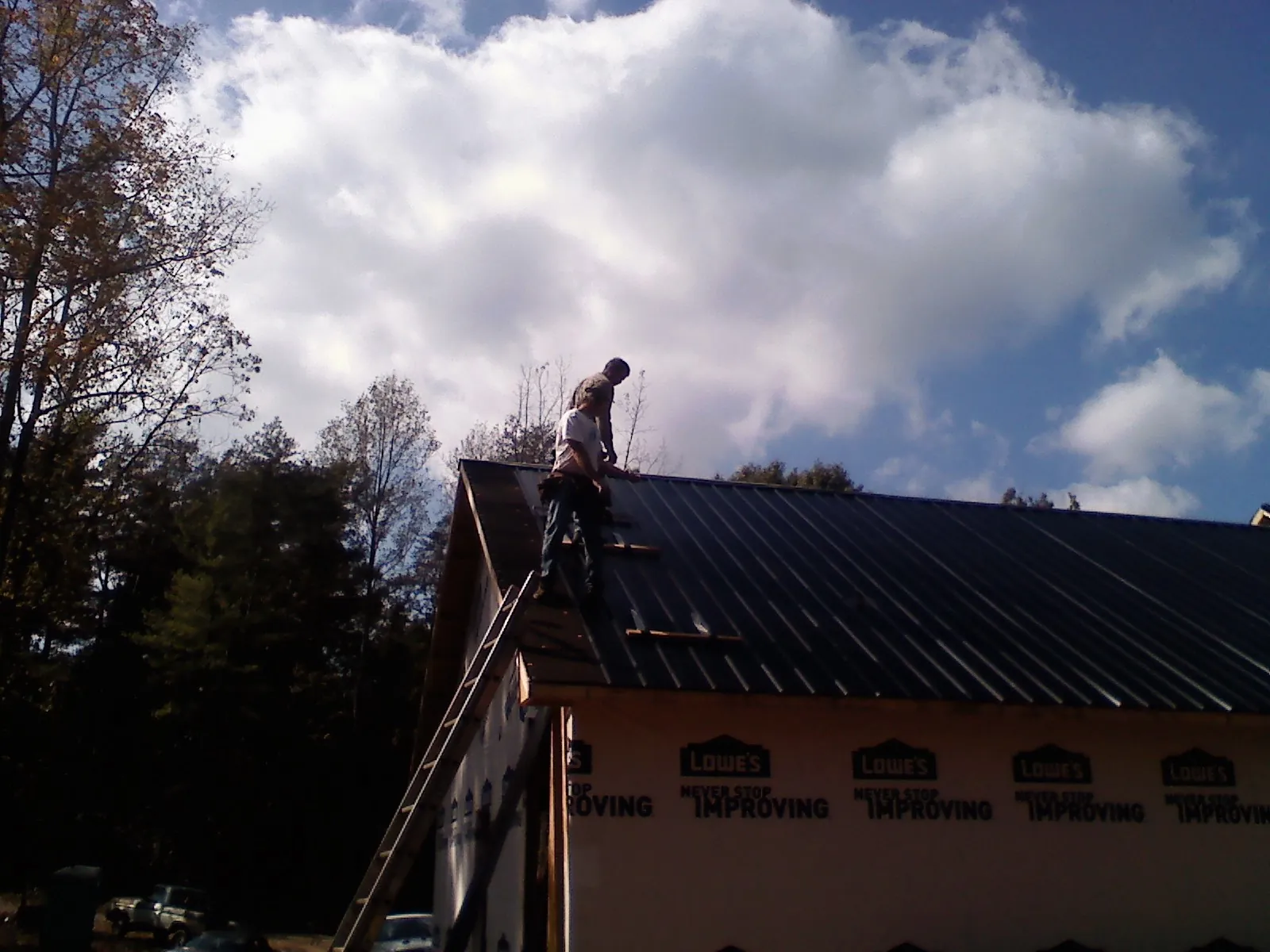 Roofer fastening dark metal panels high against a cloudy sky, from a Roof Inspection job in Mc Cool Junction