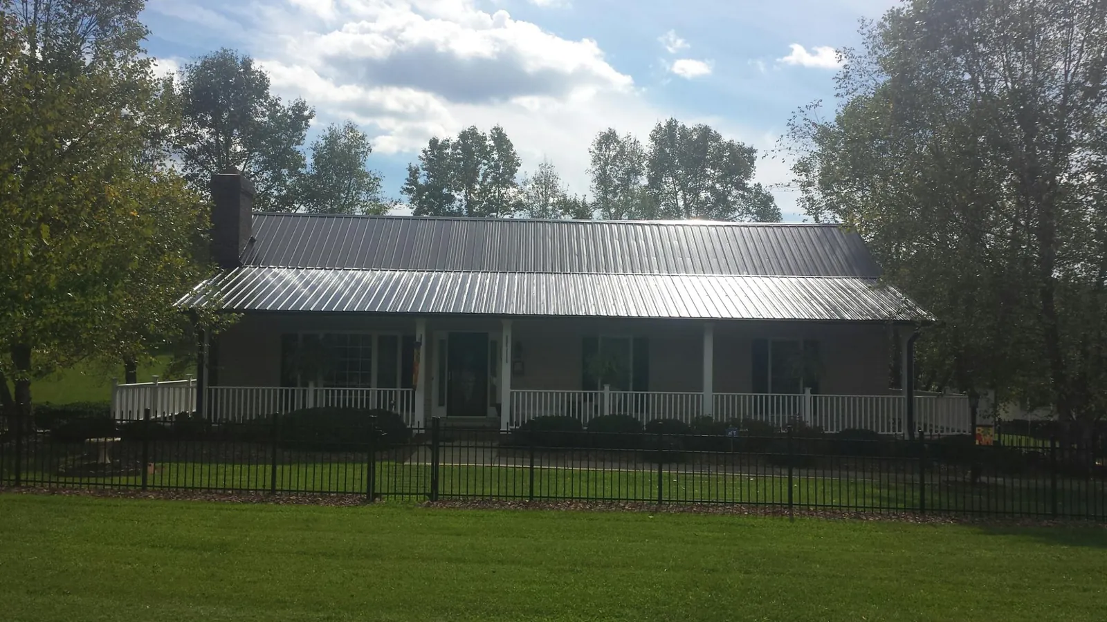 Gray metal roof on a brick ranch with a full width front porch — Gutter Guard Installation work by our crew in Mc Cool Junction