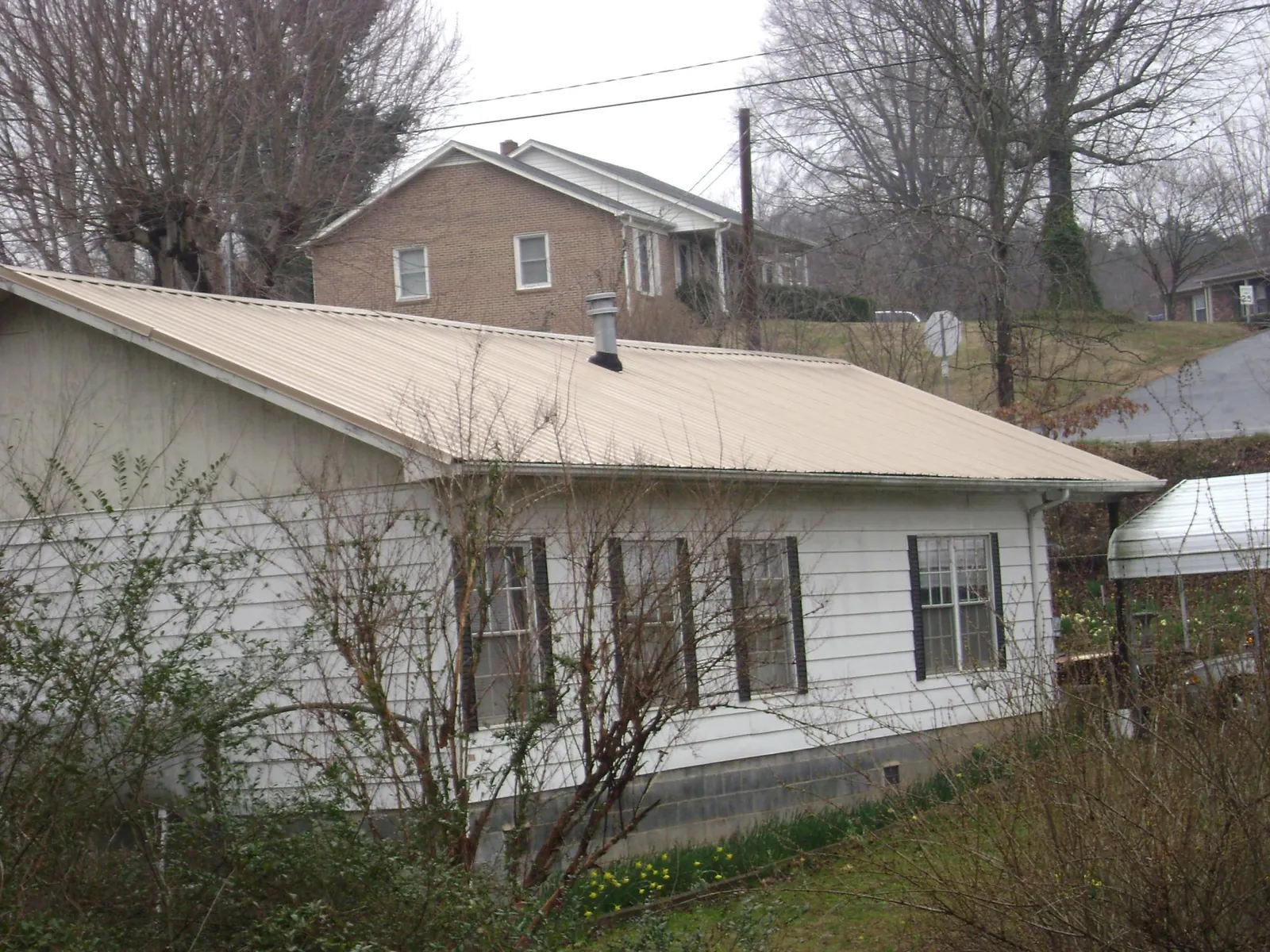 Tan metal roof on a white sided house set into a hillside — Commercial Roofing by Roofing Brothers in Mc Cool Junction